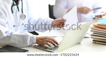 Cropped image of Researcher team working together with computer laptop and tablet while sitting at white working desk over modern laboratory as background.