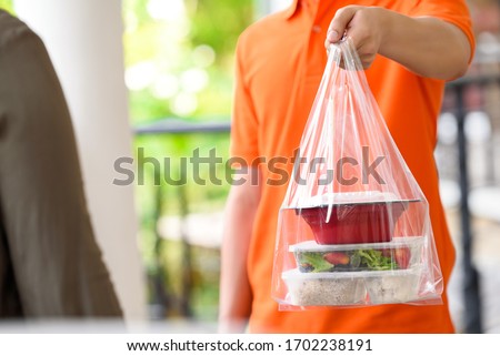 Delivery man in orange uniform delivering Asian food in takeaway boxes to customer at home Royalty-Free Stock Photo #1702238191