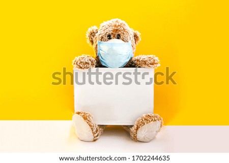 Coronavirus covid-19 and pollution protection concept. teddy bear doll wearing mask and holding lightbox with place for your text on yellow background, copy space, Medical care, Quarantine 2020