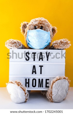 Coronavirus covid-19 and pollution protection concept. teddy bear doll wearing mask and holding lightbox with text STAY AT HOME on yellow background, copy space, Medical care, Quarantine 2020