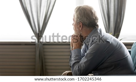 Rear view sad older man looking in window, sitting on couch at home alone, unhappy upset mature male feeling lonely and depressed, thinking about emotional or health problems, remembering past Royalty-Free Stock Photo #1702245346