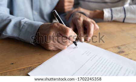 Close up older man putting signature on legal documents, mature couple, wife and husband making purchasing or investment deal, taking loan or buying new house, senior male signing contract Royalty-Free Stock Photo #1702245358