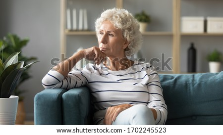 Thoughtful mature woman sitting on couch at home alone, dreaming and planning, serious pensive older senior female looking into distance, in window in living room, thinking about problems Royalty-Free Stock Photo #1702245523