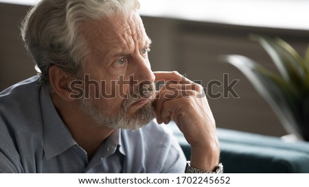 Close up unhappy pensive older man thinking about problems, lost in thoughts, looking into distance, sitting alone, sad upset mature male feeling lonely, nostalgia and melancholy Royalty-Free Stock Photo #1702245652