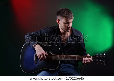 Young musician playing acoustic guitar and singing, on dark color background