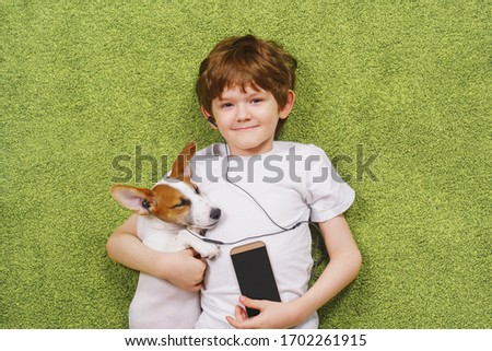 Little boy with a dog listen to music on the phone while lying on the carpet. Friendship, stay home concept. Royalty-Free Stock Photo #1702261915