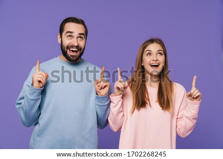 Picture of a happy cheerful young loving couple isolated over purple background pointing.