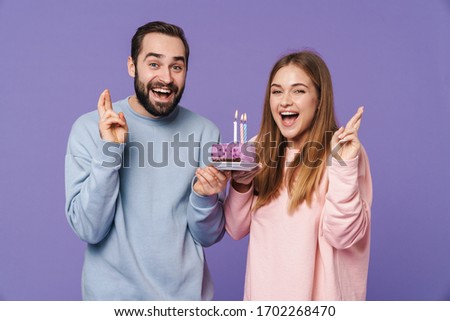 Image of a positive optimistic young loving couple isolated over purple wall background with birthday cake showing wish gesture.