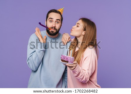 Image of a positive optimistic young loving couple isolated over purple wall background with birthday cake.