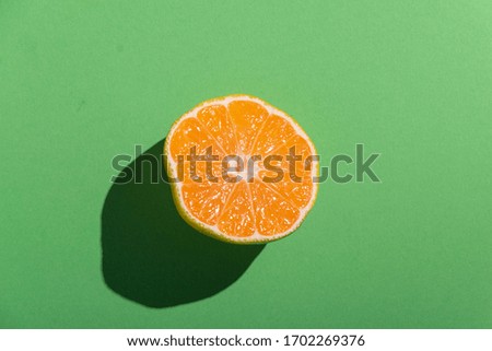 a half of fresh ripe mandarin with strong shadow on a green background 