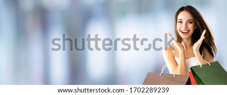 Shopping woman. Happy excited girl, holding bags, over blurred mall background. Copy space for some slogan or sign text. Consumerism and sales ad concept picture. Wide banner composition. 