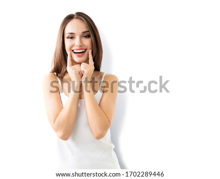 Brunette lovely young woman pointing at smile, isolated over white background. Beautiful girl in emoshions and optimistic, positive, happy feeling concept. Dental health concept picture.