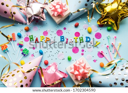 Text Happy Birthday by wooden  letters with birthday asseccories, candles and confetti  on blue background