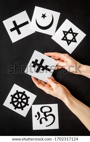 Choose religion concept. Hands with Orthodox cross near world religions symbols on black background top view
