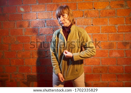 A middle-aged woman poses showing clothes near red brick wall. An inept model in non-professional shooting. Photography for sales short cardigan on the Internet or online store