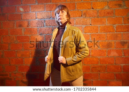 A middle-aged woman poses showing clothes near red brick wall. An inept model in non-professional shooting. Photography for sales short cardigan on the Internet or online store