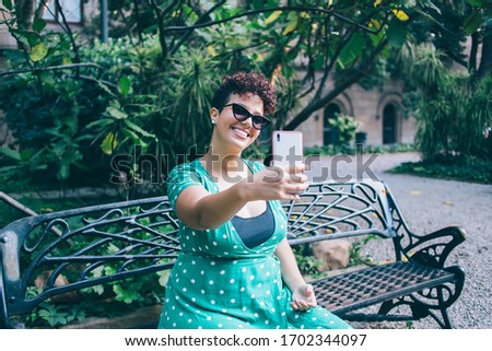 Happy woman in trendy sunglasses posing for clicking selfie images and share to social networks for popularize travel blog, cheerful Spanish female influencer smiling at front smartphone camera