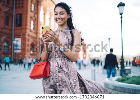 Joyful female tourist using cellular technology for creating content publication with web guide for visiting Moscow city, pretty woman with smartphone reading positive message during online chatting