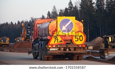 Watering machine, water tanker truck with orange barrel and road signs near the construction site
