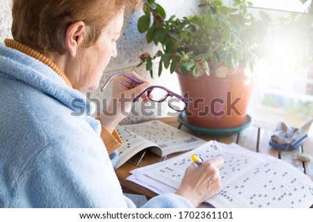 senior woman doing crossword puzzles or hobbies sitting Royalty-Free Stock Photo #1702361101