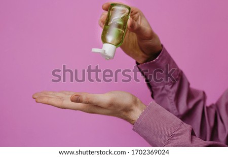 The guy treats his hands with an antibacterial sanitizer. Pink background. Medical content