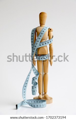 Isolated wood adjustable mannequin holding and wrapped in a blue tape measure for a weight loss and plastic surgery beauty concept Royalty-Free Stock Photo #1702373194