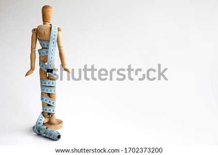 Isolated wood adjustable mannequin wrapped in a blue tape measure for a weight loss and plastic surgery beauty concept Royalty-Free Stock Photo #1702373200