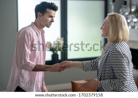 Appointment. Blond psychologist shaking hands her young male patient in her office and smiling
