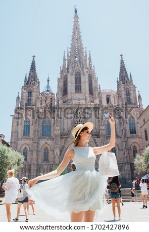 Young and happy tourist woman making selfie photo in front of cathedral in Barcelona