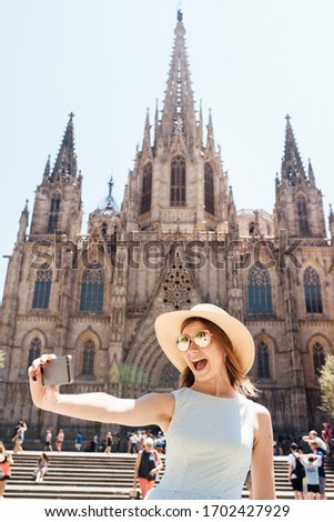 Young and happy tourist woman making selfie photo in front of cathedral in Barcelona