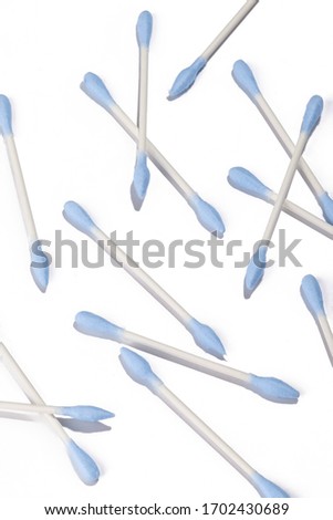 Subject shot of a plenty of double tipped bamboo cotton swabs with blue pointy and oval applicators. The cotton sticks are spread all over the white surface. 