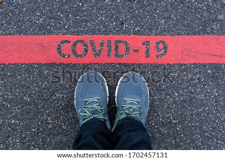 man in sneakers standing next to a red line with text COVID-19, restriction or safety warning concept Royalty-Free Stock Photo #1702457131