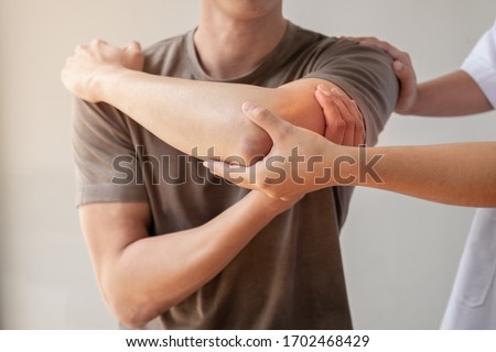 Female physiotherapists provide assistance to male patients with elbow injuries examine patients in rehabilitation centers. Physiotherapy concepts. Royalty-Free Stock Photo #1702468429