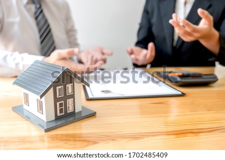 A real estate agent with House model is talking to clients about buying home insurance. Home insurance concept.