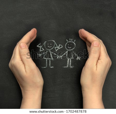 Hands protect children drawn on blackboard with chalk. Concept for International Children's Day, June 1. Royalty-Free Stock Photo #1702487878