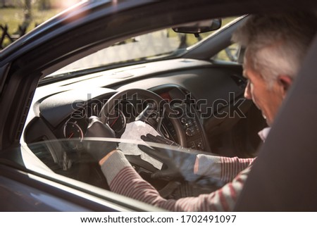 Senior man wearing black protective gloves disinfecting the inside of a car with antibacterial wet wipes.