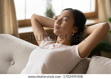 Close up image asian ethnicity millennial woman resting leaned on couch in living room. Breath fresh air, reduce fatigue, enjoy weekend free time at modern home alone, no stress inner harmony concept Royalty-Free Stock Photo #1702499308