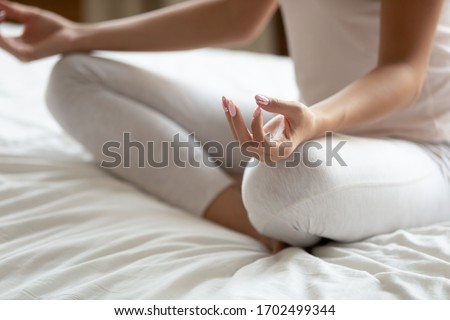 Close up view woman in casual home clothes seated with crossed legged lotus position do meditation practice folded fingers as sign of harmony. No stress, healthy life habits, new day with yoga concept Royalty-Free Stock Photo #1702499344