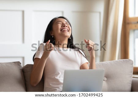 Asian young excited woman sit on couch hold notebook on lap feels overjoyed received great news by e-mail message. University admission passed exams scholarship, lottery win, dating invitation concept Royalty-Free Stock Photo #1702499425