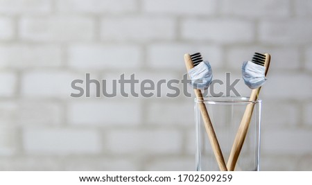  loving couple in medical masks on quarantine. self-isolation and love concept. Two toothbrushes in the glass over brick wall background. Bamboo eco friendly toothbrushes with protective masks