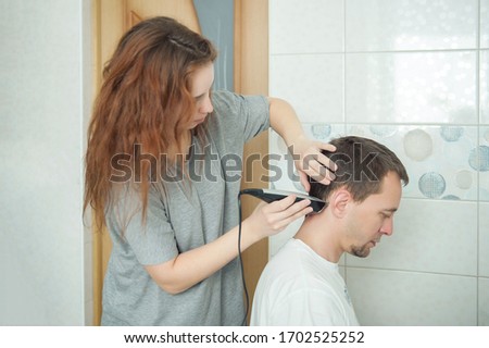 young woman cuts hair to young man in the bathroom at home. home care for the hairs. forced measures. hair cutting at home. non-professional hairdresser. Royalty-Free Stock Photo #1702525252