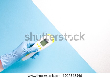 hand in blue disposable rubber glove holds infrared non-contact thermometer against the background of the american flag, coronavirus pandemic in the usa concept