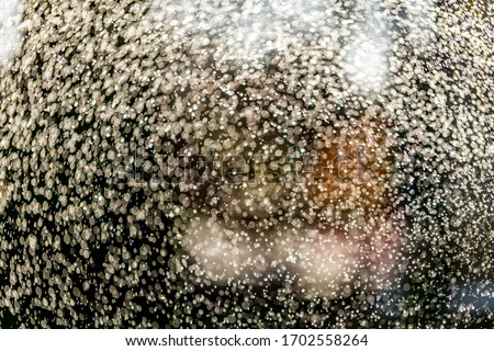 Abstract splashes of water on bokeh background in sunshine. Freeze motion of white particles. Rain, snow overlay texture.