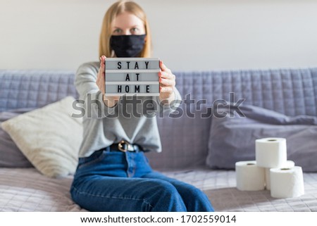 Pandemic Covid-19 Coronavirus. Stay Work at home, social distance. quarantined woman sitting on the sofa and showing text stay at home on white lightbox. Stop virus. Quarantine at home.