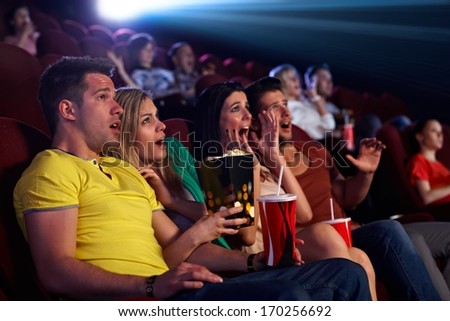 Audience sitting in multiplex movie theater, watching horror movie, screaming.