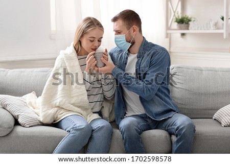 Care about infected spouse. Caring husband bringing cup of tea to his sick wife at home Royalty-Free Stock Photo #1702598578