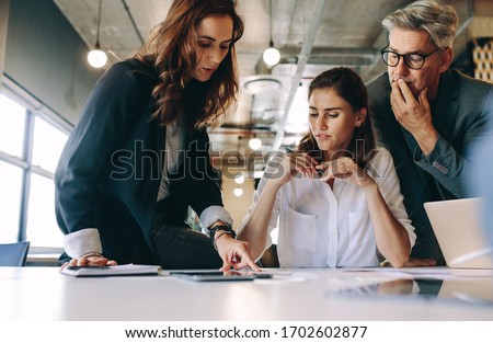 Businesswoman discussing new strategies with her team sitting around a table. Group of business people having a meeting on new project in office. Royalty-Free Stock Photo #1702602877
