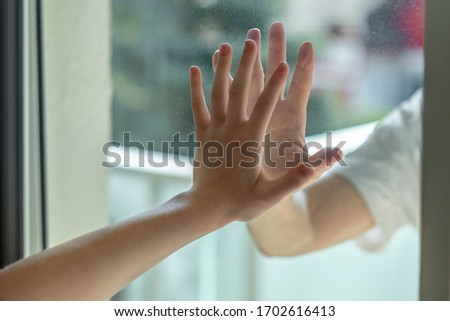 Hands separated by a glass window for social distancing during the corona virus lockdown Royalty-Free Stock Photo #1702616413