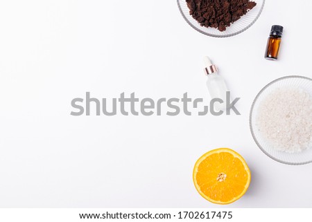 Natural ingredients for homemade scrub with ground coffee, sea salt, orange essential oil and moisturizing serum, flat lay on white background with copy space.