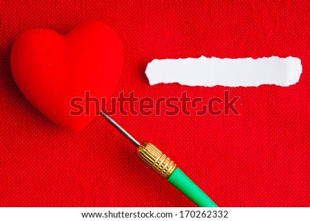 Piece scrap of white paper blank copy space and hearts symbols of love with green dart on red fabric textile material background. Valentine's day.